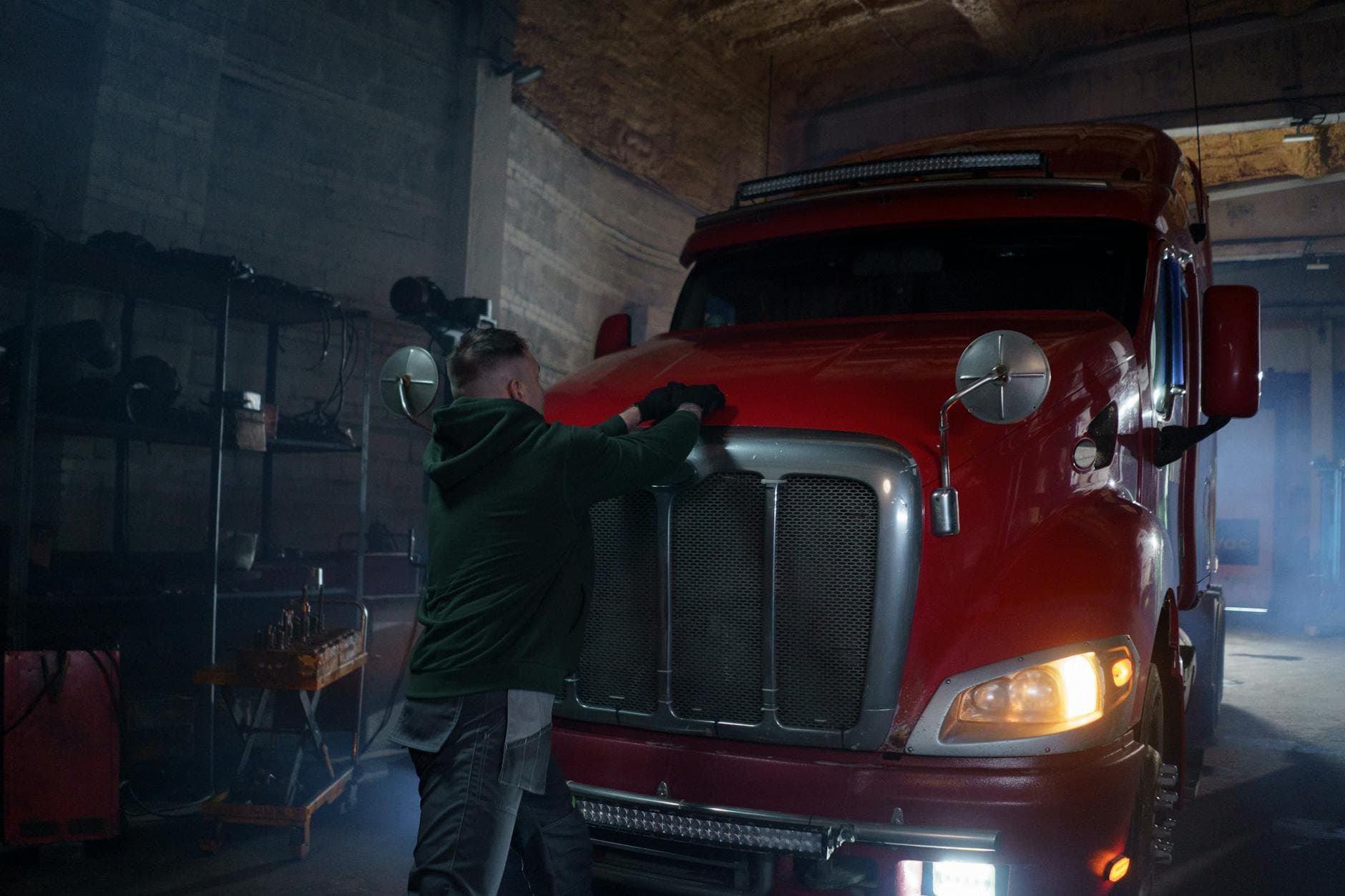 A mechanic working under the raised hood of a semi truck in a garage.
