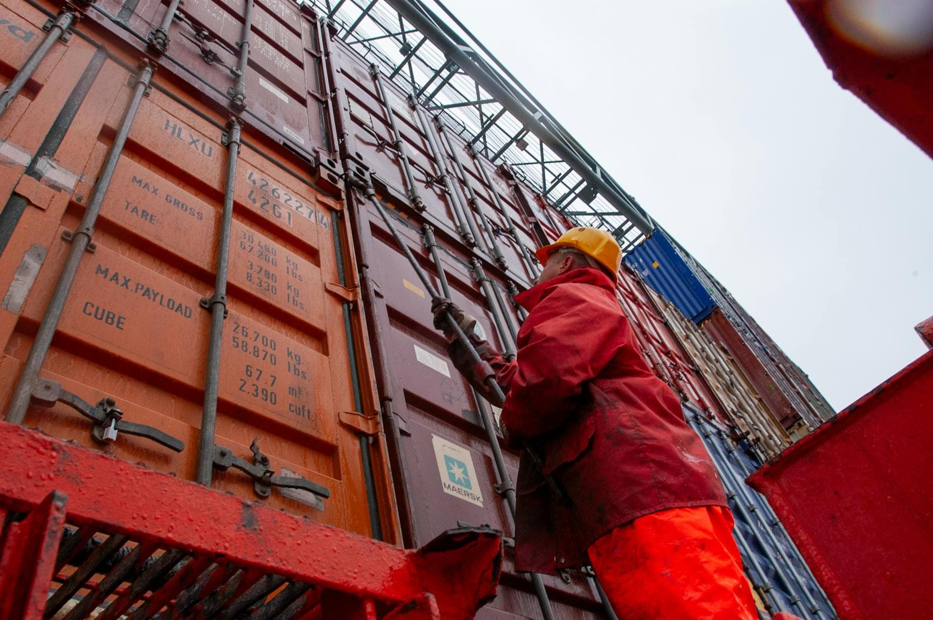 A port worker in foul-weather gear securing stacked shipping containers.