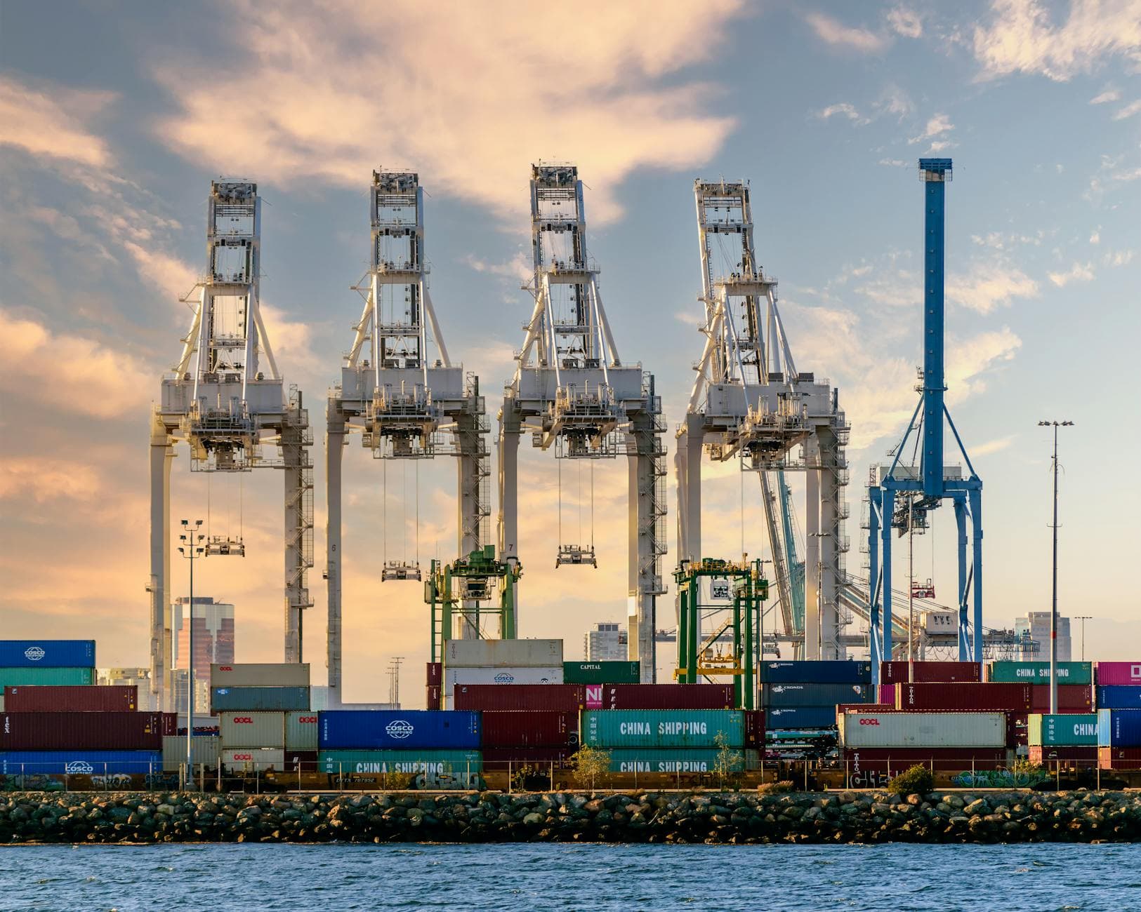 Ship-to-shore gantry cranes over shipping containers at a marine terminal.