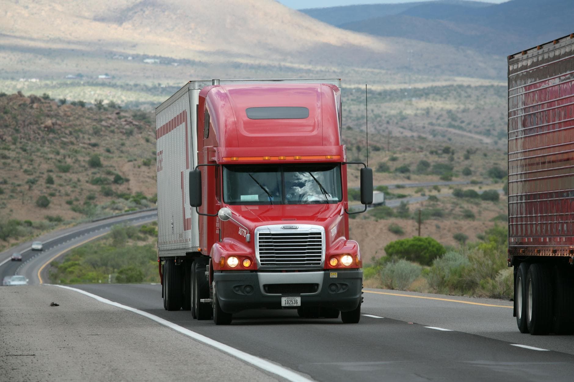 A semi truck hauling freight on a highway through mountainous terrain.